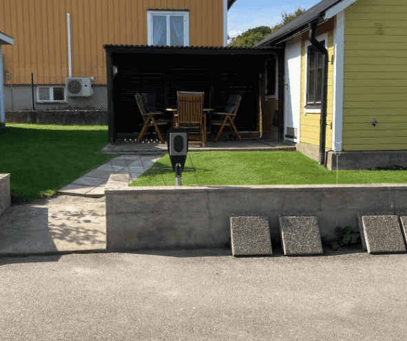 Diskret laddstolpe placerad vid villatomt med pergola